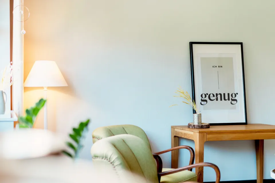 Lichtdurchflutete Sitzecke mit grünen Sesseln und dem Bild „Ich bin genug“